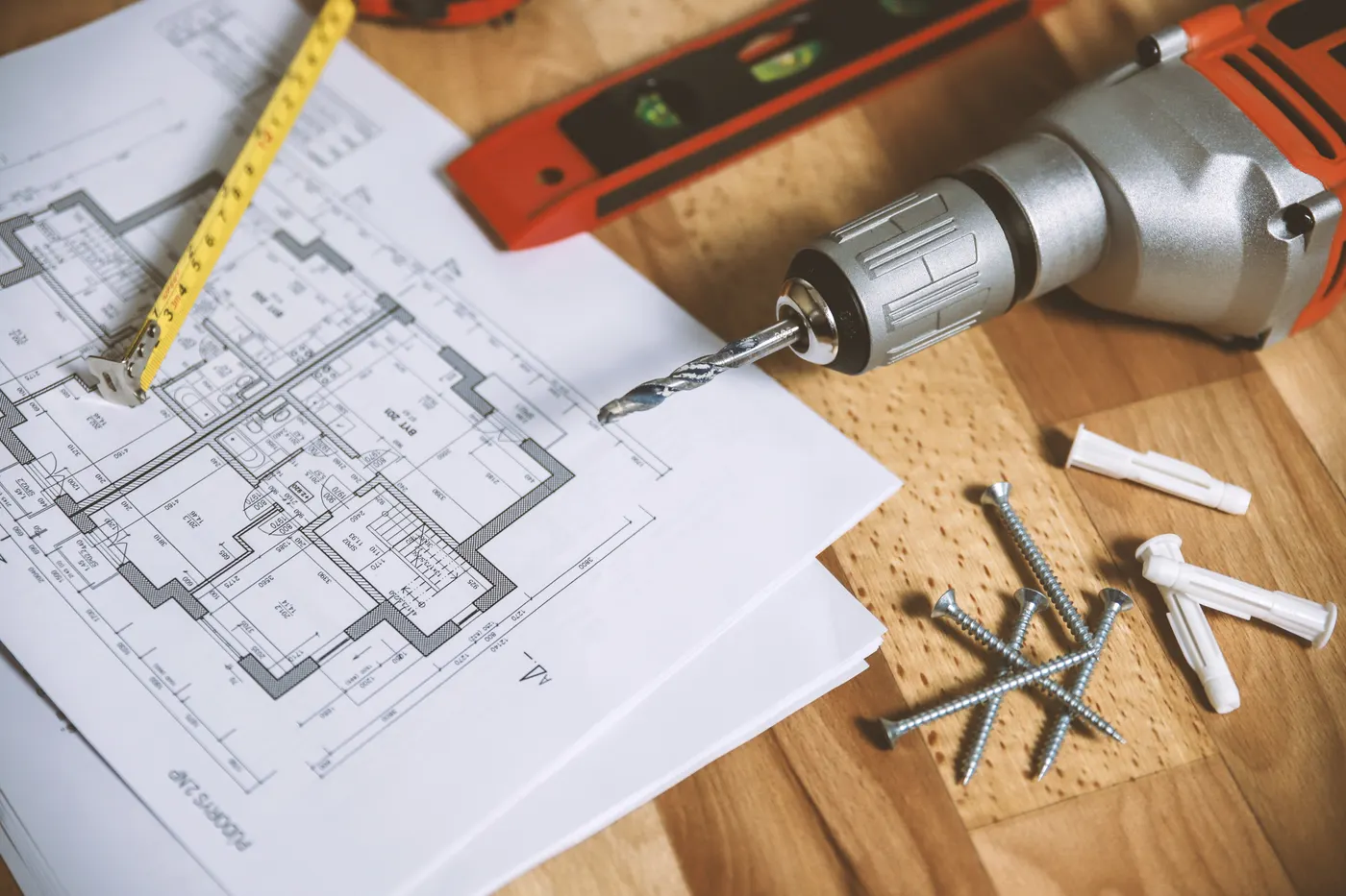 House plans on a workbench with a drill, tape measure and level