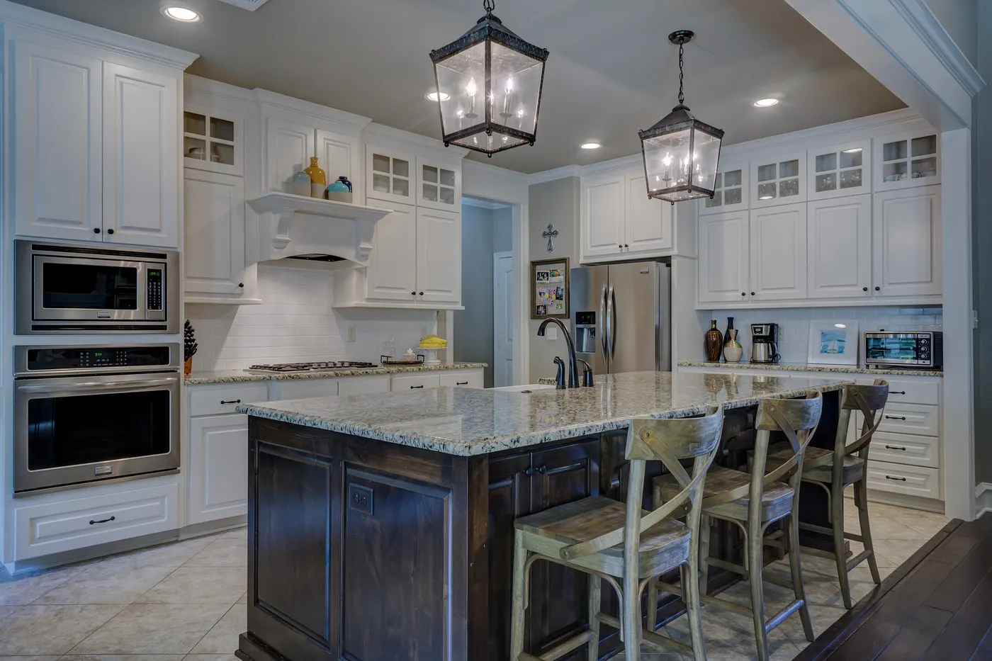 A remodeled kitchen with white cabinets, a dark island and pendant lights