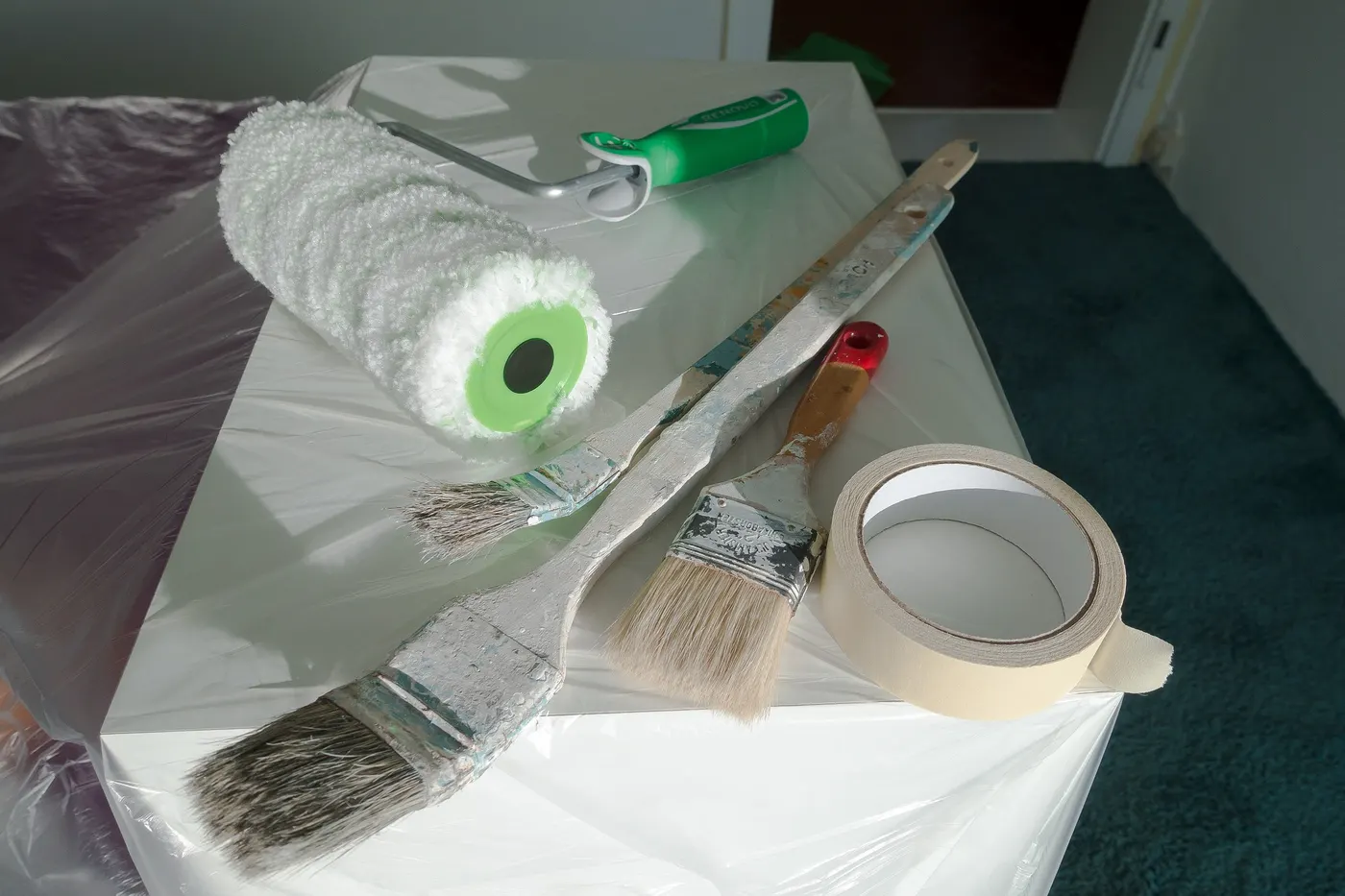 A paint roller, brushes and tape on a drop cloth